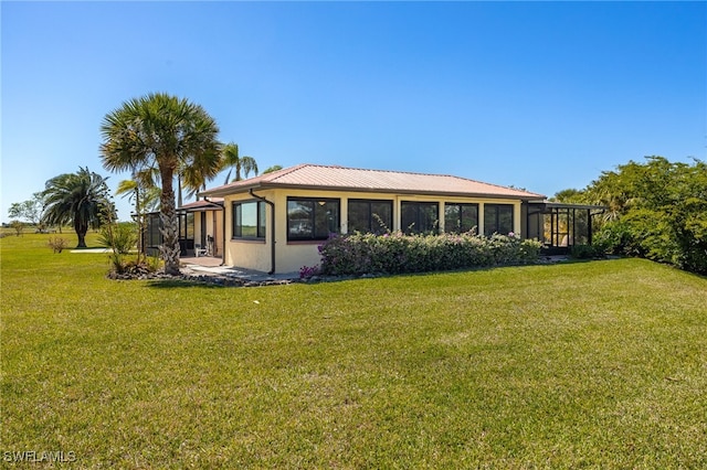 rear view of house with glass enclosure, a lawn, and stucco siding