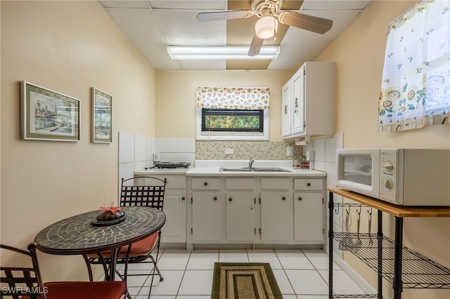 kitchen with a sink, decorative backsplash, white microwave, and light tile patterned flooring