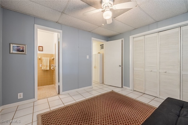 bedroom featuring light tile patterned floors, a ceiling fan, a closet, and a drop ceiling