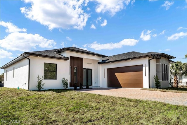 prairie-style home with stucco siding, a front lawn, decorative driveway, and a garage