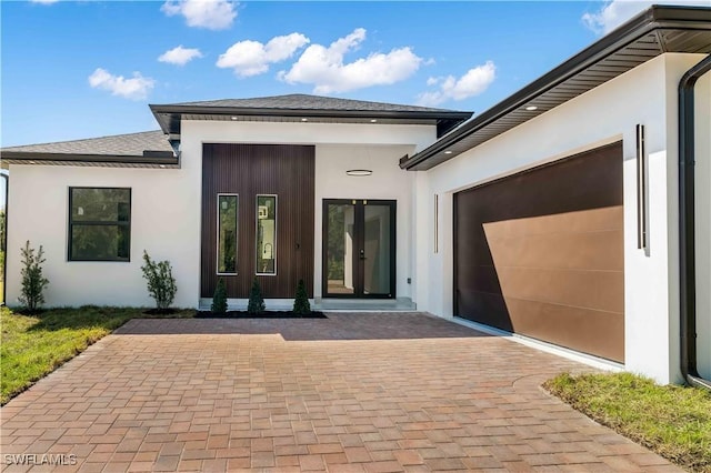 property entrance with stucco siding, french doors, an attached garage, and decorative driveway