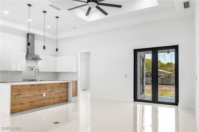 kitchen with visible vents, white cabinetry, a raised ceiling, wall chimney exhaust hood, and modern cabinets