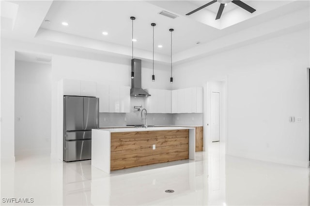 kitchen featuring visible vents, wall chimney range hood, freestanding refrigerator, white cabinetry, and modern cabinets