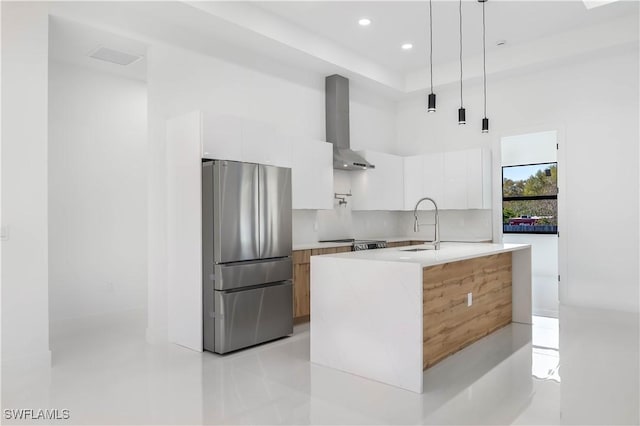 kitchen featuring modern cabinets, freestanding refrigerator, wall chimney exhaust hood, white cabinets, and light countertops