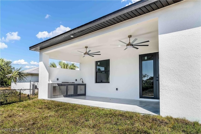 view of patio with exterior kitchen, a ceiling fan, and fence