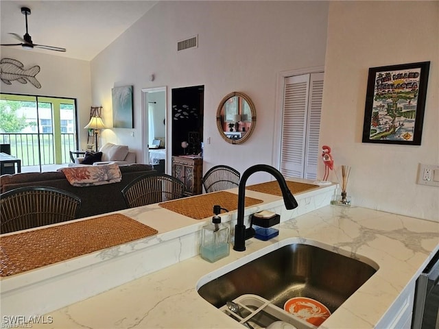 kitchen with visible vents, high vaulted ceiling, a sink, open floor plan, and light stone countertops