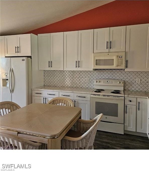 kitchen with backsplash, light countertops, vaulted ceiling, white appliances, and white cabinetry