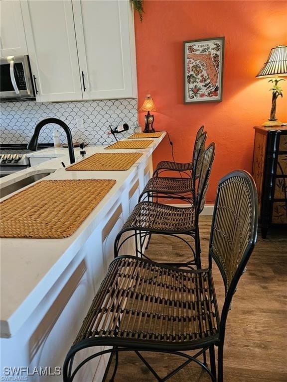 kitchen with stainless steel microwave, light countertops, decorative backsplash, wood finished floors, and a sink