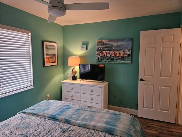 bedroom with ceiling fan, baseboards, multiple windows, and dark wood finished floors