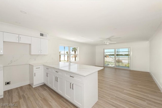 kitchen with visible vents, light stone countertops, a peninsula, light wood-style floors, and white cabinetry