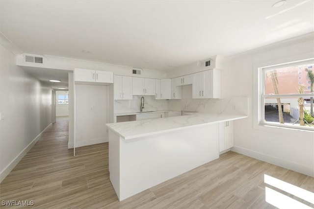 kitchen featuring light stone countertops, visible vents, a peninsula, a sink, and decorative backsplash