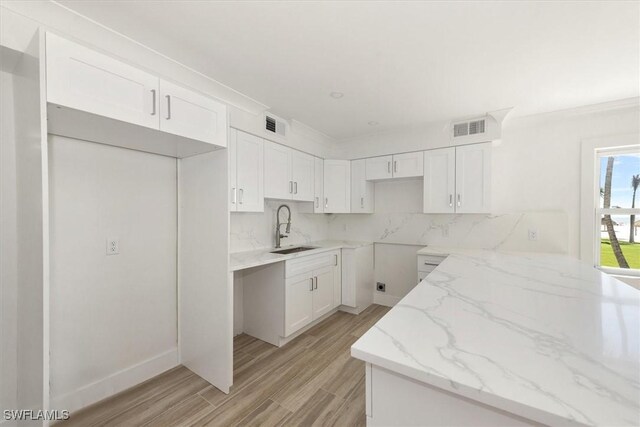 kitchen with light stone counters, visible vents, white cabinetry, and a sink