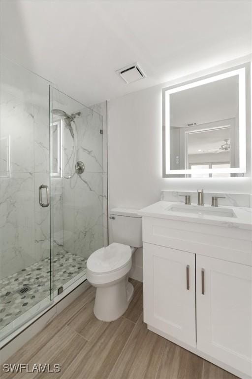 full bath featuring visible vents, toilet, wood finished floors, a marble finish shower, and vanity