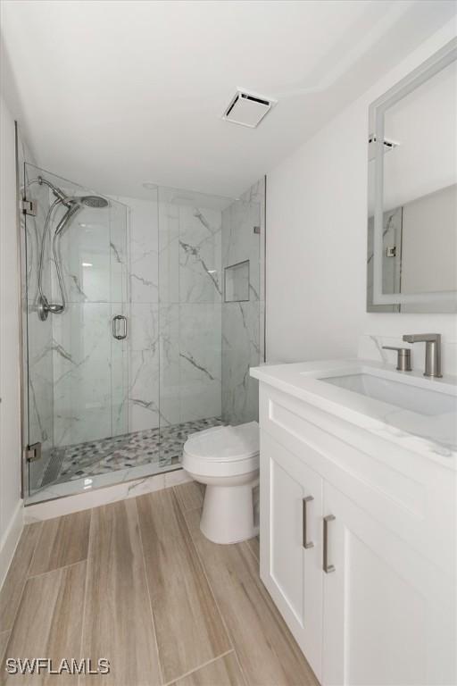 bathroom with visible vents, toilet, wood finished floors, a marble finish shower, and vanity