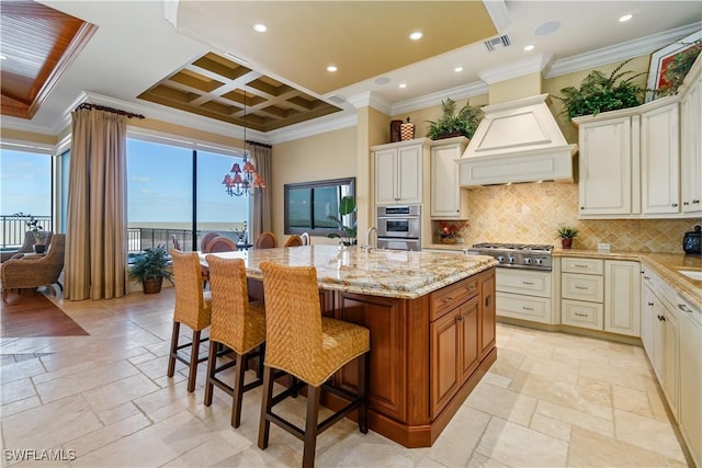 kitchen with stone tile floors, light stone countertops, coffered ceiling, custom exhaust hood, and stainless steel appliances