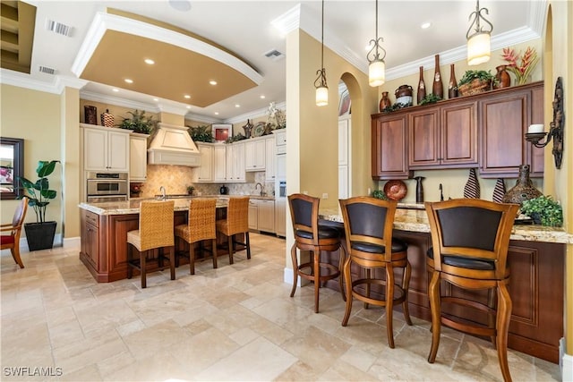 kitchen featuring custom range hood, light stone counters, a breakfast bar area, and visible vents