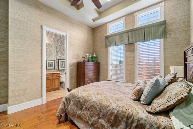 bedroom featuring baseboards, light wood-style floors, ensuite bath, and a ceiling fan