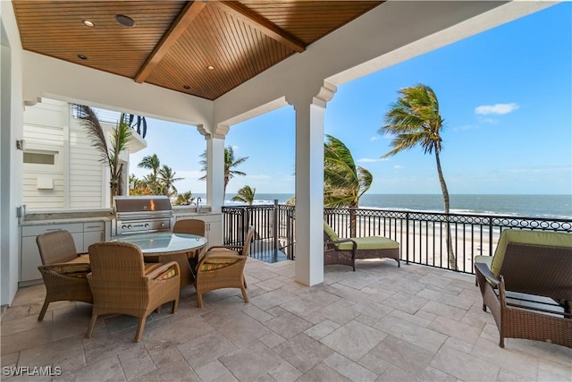 view of patio / terrace featuring outdoor dining area, a water view, a grill, and an outdoor kitchen