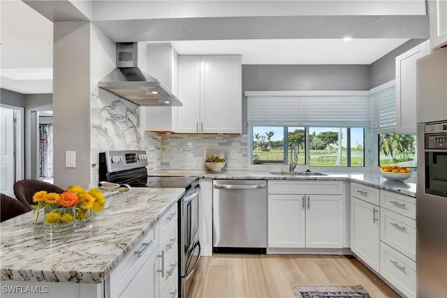 kitchen featuring a sink, backsplash, appliances with stainless steel finishes, wall chimney range hood, and light stone countertops