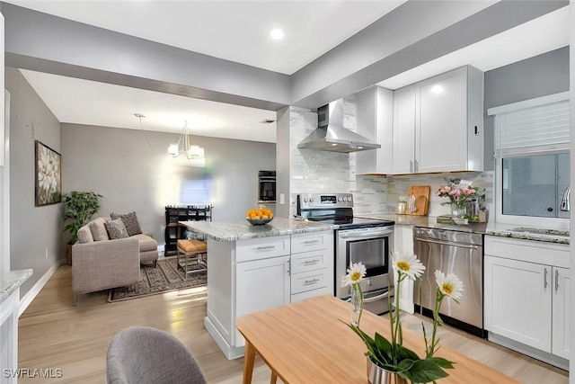 kitchen with a sink, decorative backsplash, stainless steel appliances, wall chimney exhaust hood, and a notable chandelier