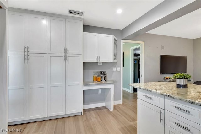 kitchen featuring light stone counters, visible vents, baseboards, light wood-style floors, and white cabinetry