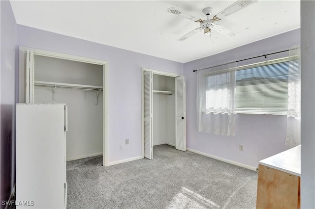 unfurnished bedroom featuring carpet flooring, baseboards, multiple closets, and a ceiling fan