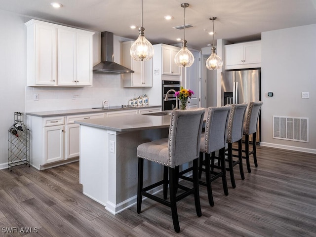 kitchen featuring visible vents, a sink, stainless steel appliances, wall chimney exhaust hood, and a kitchen island with sink