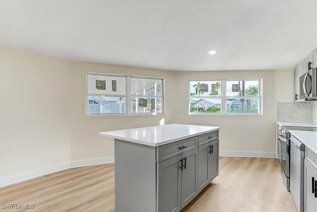kitchen with light wood-style flooring, gray cabinets, stainless steel appliances, light countertops, and baseboards