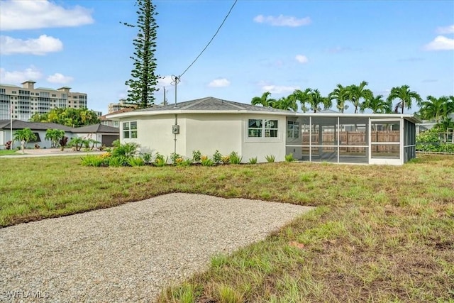 back of property with a sunroom, stucco siding, and a lawn