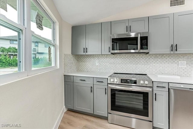 kitchen with vaulted ceiling, a wealth of natural light, gray cabinetry, and stainless steel appliances