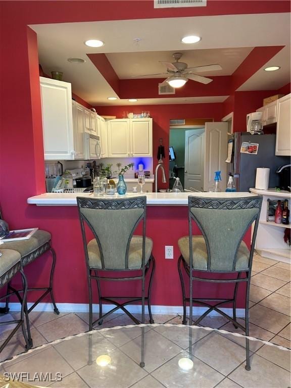 kitchen featuring visible vents, a kitchen breakfast bar, freestanding refrigerator, light tile patterned flooring, and white microwave