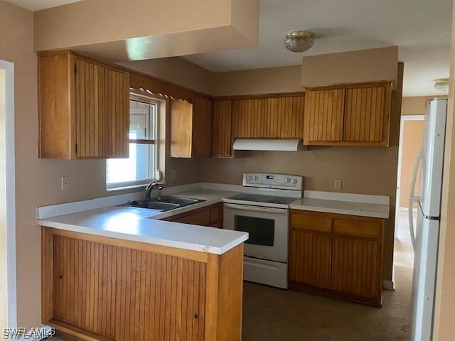 kitchen featuring under cabinet range hood, light countertops, a peninsula, white appliances, and a sink