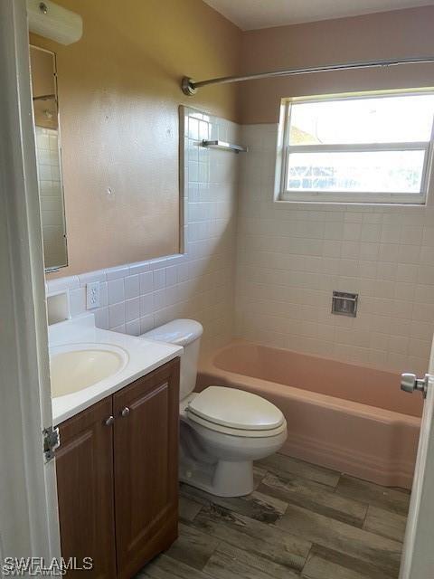 bathroom with vanity, wood finished floors, bathing tub / shower combination, tile walls, and toilet