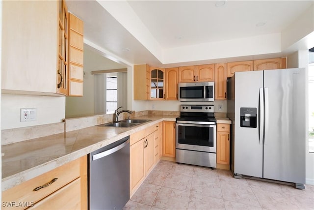 kitchen with light brown cabinetry, appliances with stainless steel finishes, glass insert cabinets, and a sink