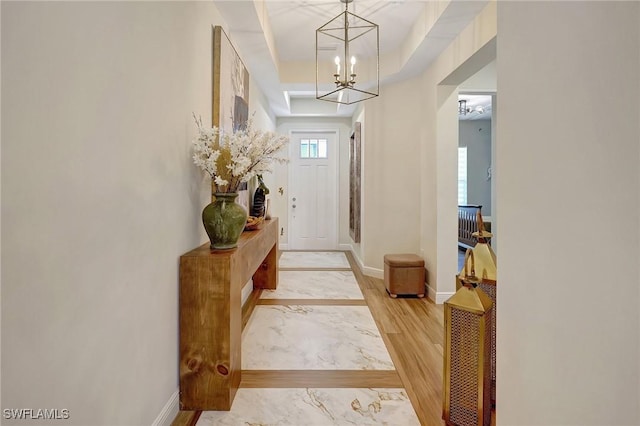 foyer entrance with baseboards, a raised ceiling, an inviting chandelier, and wood finished floors