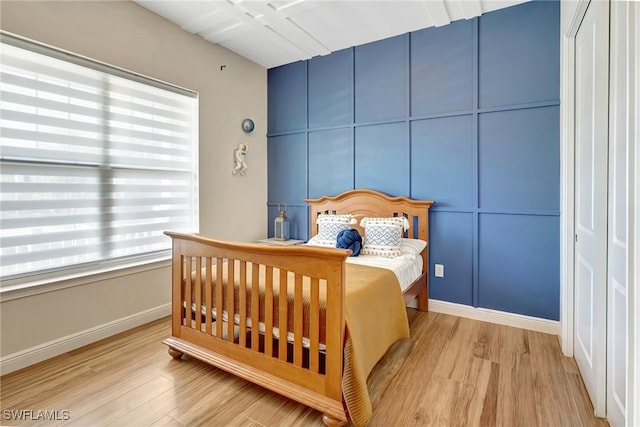 bedroom featuring a decorative wall, wood finished floors, and baseboards