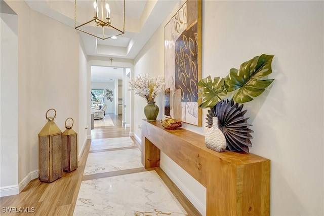 corridor featuring a tray ceiling, baseboards, and wood finished floors