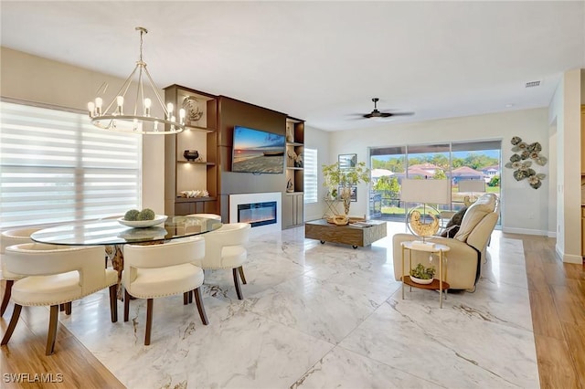 dining area with visible vents, baseboards, ceiling fan with notable chandelier, a glass covered fireplace, and marble finish floor