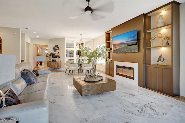 living room featuring visible vents, built in shelves, ceiling fan with notable chandelier, a glass covered fireplace, and marble finish floor