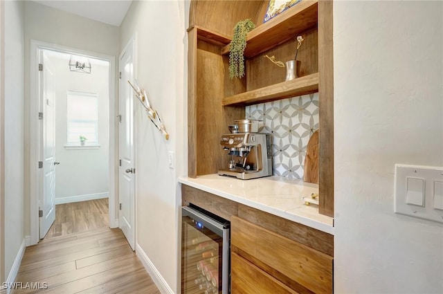 bar with beverage cooler, baseboards, decorative backsplash, a bar, and light wood-type flooring