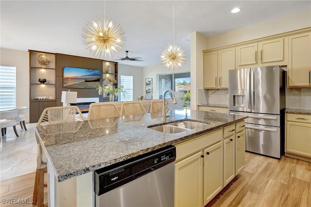 kitchen with an island with sink, a sink, cream cabinets, stainless steel appliances, and decorative backsplash