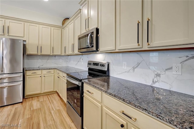 kitchen featuring backsplash, light wood-style flooring, dark stone countertops, cream cabinetry, and stainless steel appliances