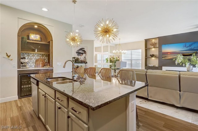 kitchen featuring a sink, light wood-type flooring, a center island with sink, and dark stone counters