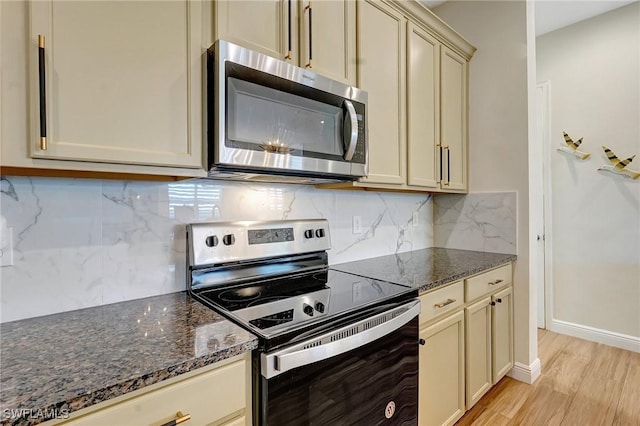 kitchen with dark stone counters, decorative backsplash, light wood-style floors, appliances with stainless steel finishes, and cream cabinets