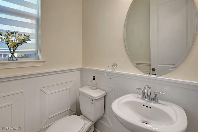 half bathroom with a decorative wall, toilet, wainscoting, and a sink