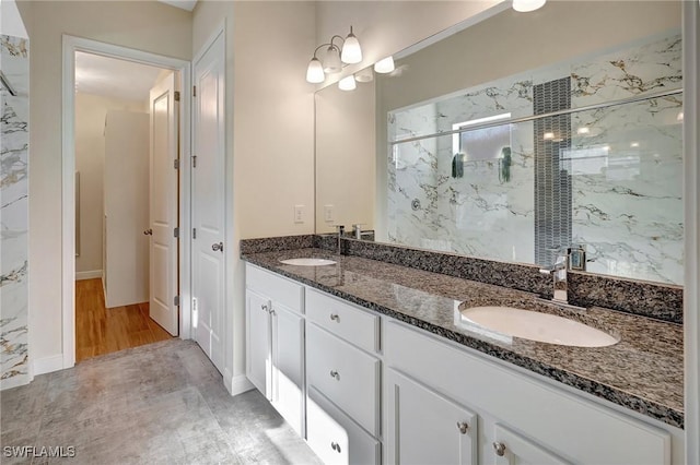 bathroom featuring a sink, a marble finish shower, and double vanity