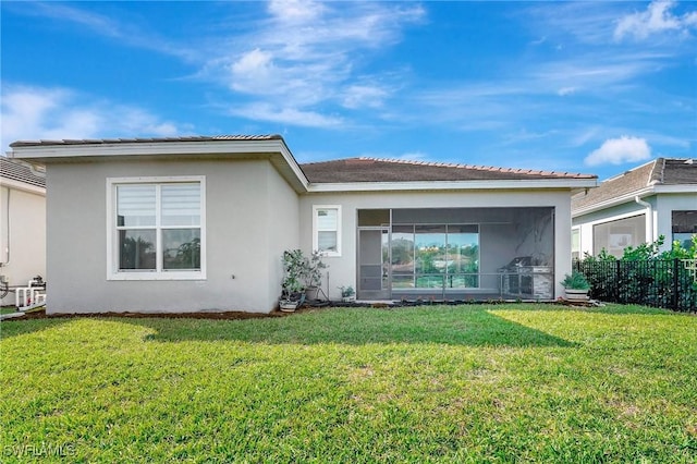 back of property with stucco siding, a lawn, fence, and a sunroom