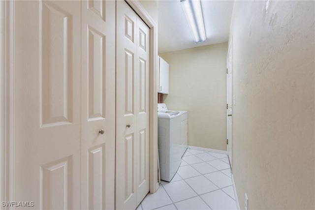 clothes washing area featuring washing machine and clothes dryer, light tile patterned floors, and cabinet space