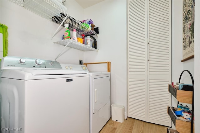 clothes washing area with separate washer and dryer, light wood-style flooring, and laundry area