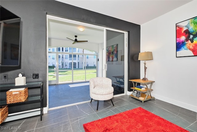 living area featuring dark tile patterned floors, baseboards, and ceiling fan